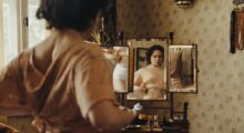 A young woman adjusts her crop top in front of a mirror.